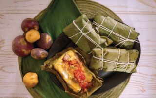 Tamales de papa envueltos en hoja de plátano, uno abierto con guiso, huevo y chicharrón